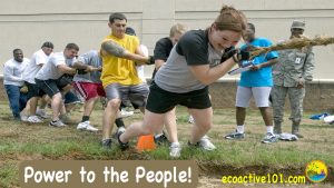 Men and women, all ethnicities, even military, pulling rope in tug of war.